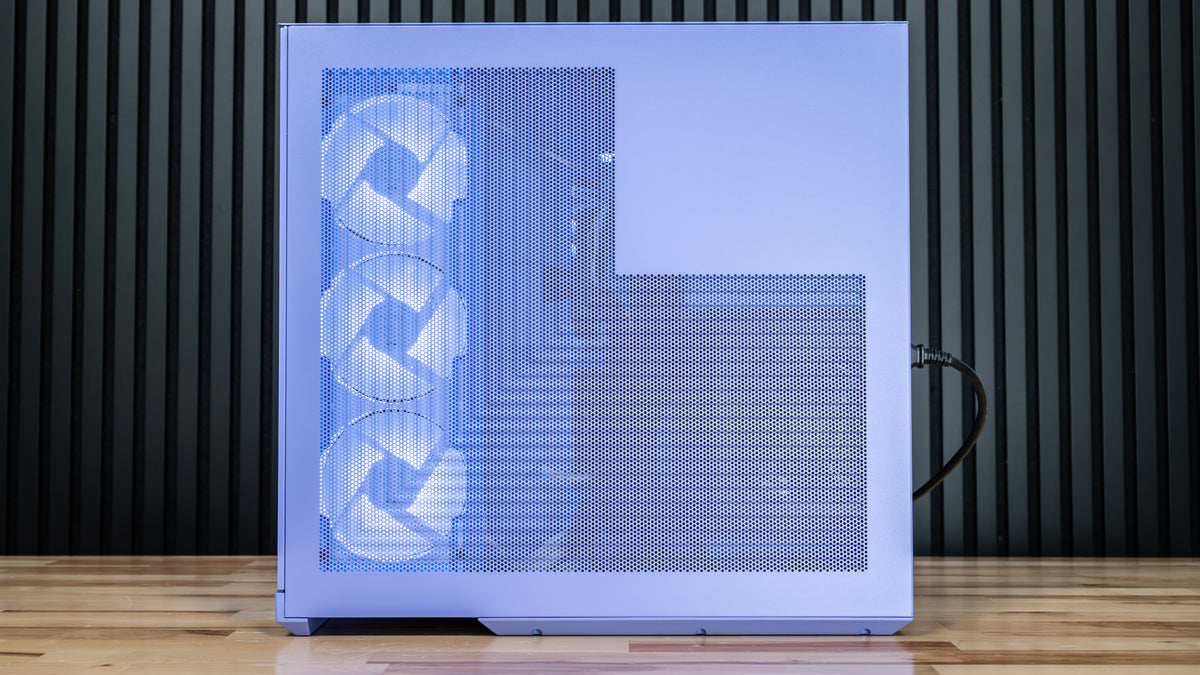 A white computer case with a blue LED interior light, featuring three front fans and a mesh front panel, standing on a wooden floor against a dark slatted wall.