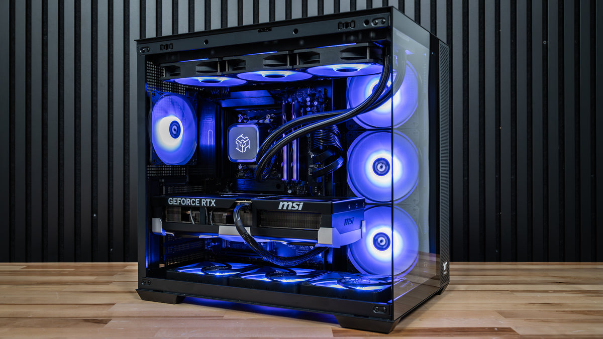 Front three-quarter view of the PowerGPU Azul AMD Ryzen RTX 5090 gaming PC on a wood desk with blue ARGB fans, 360mm liquid cooler and MSI RTX 5090 graphics card