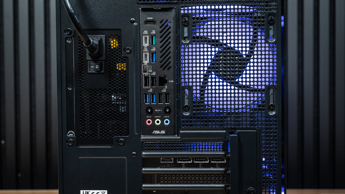 Rear view of the PowerGPU Azul RTX 5090 gaming PC showing ASUS X870 motherboard I/O ports, RTX 5090 DisplayPort and HDMI outputs, power supply and blue-lit rear exhaust fan